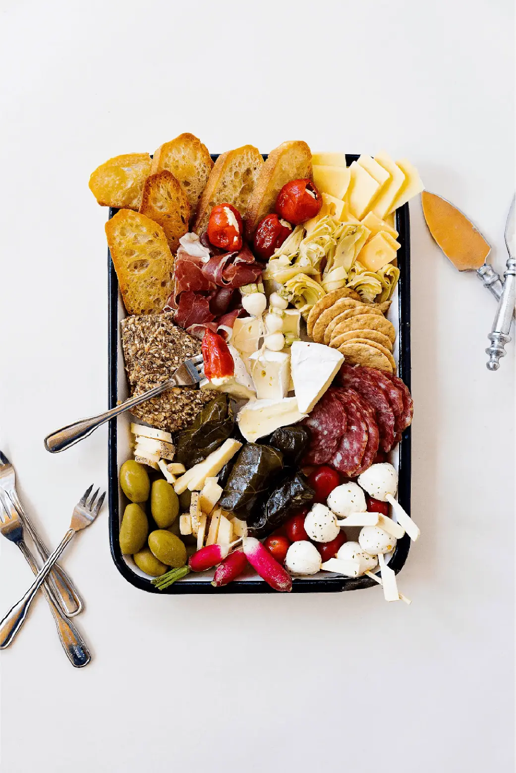 A charcuterie board with meats, cheeses, olives, pickles and bread on a white background