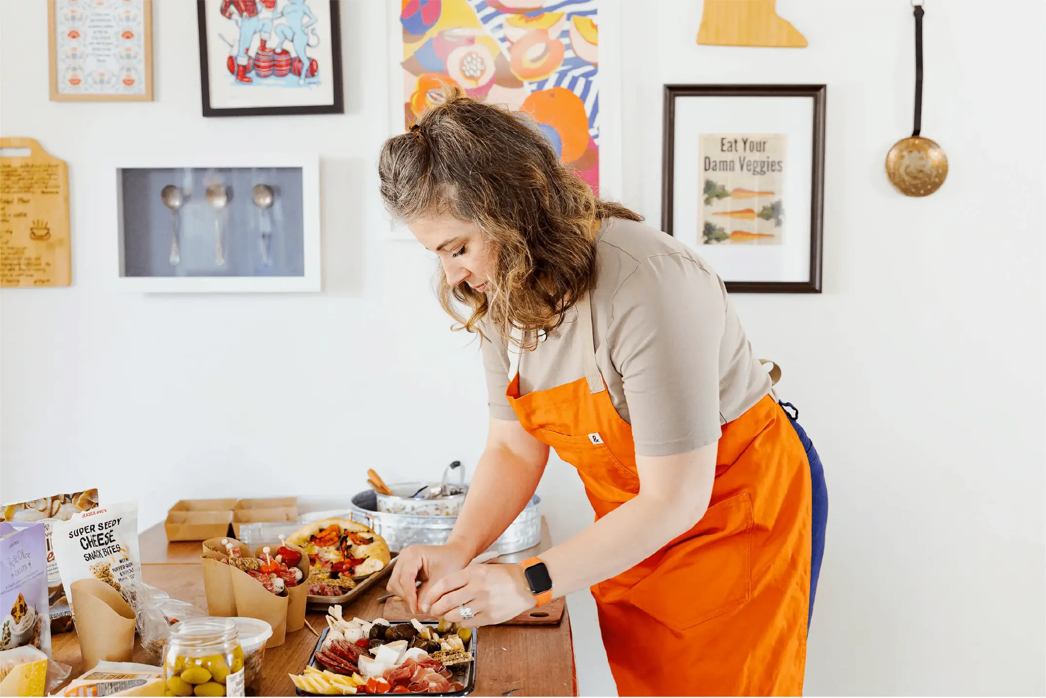 A woman in an orange apron preparing a charcuterie board